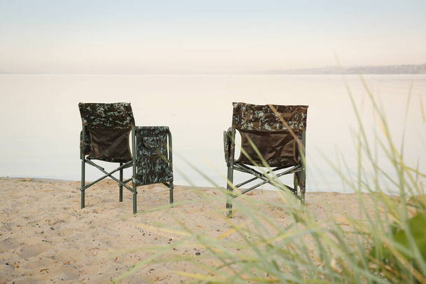Camouflage fishing chairs on sandy beach near river - Zdjęcie, obraz