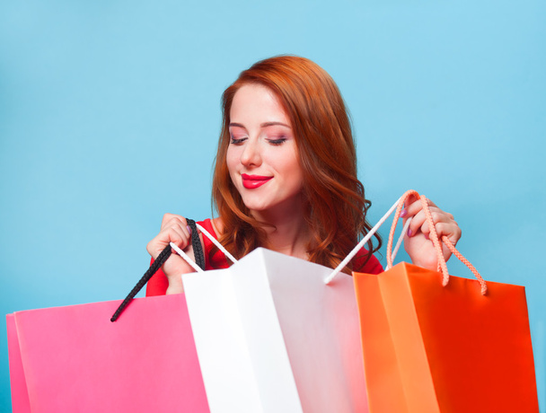 Redhead girl with shopping bags on blue background. - 写真・画像
