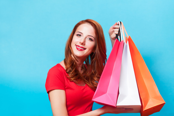 Redhead girl with shopping bags on blue background. - Photo, Image
