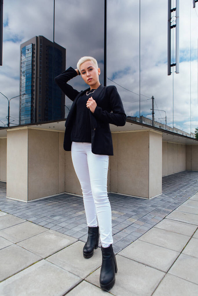 Young stylish business woman with short hair and nose piercing. Confident girl look like lesbian standing near business center with mirror walls - Foto, Bild