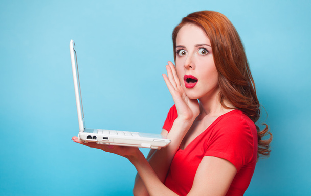 Redhead girl with laptop on blue background. - 写真・画像