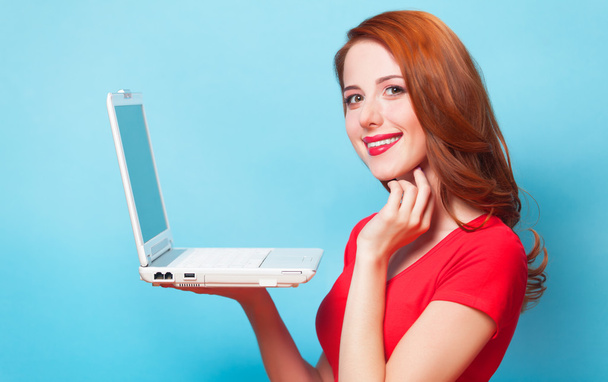 Redhead girl with laptop on blue background. - Foto, afbeelding