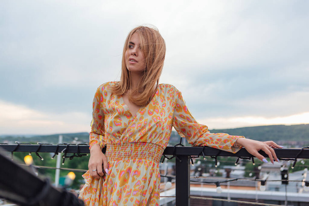 Beautiful young woman in long leopard dress standing on the stairs on the top of the roof of a building. - Foto, Imagen