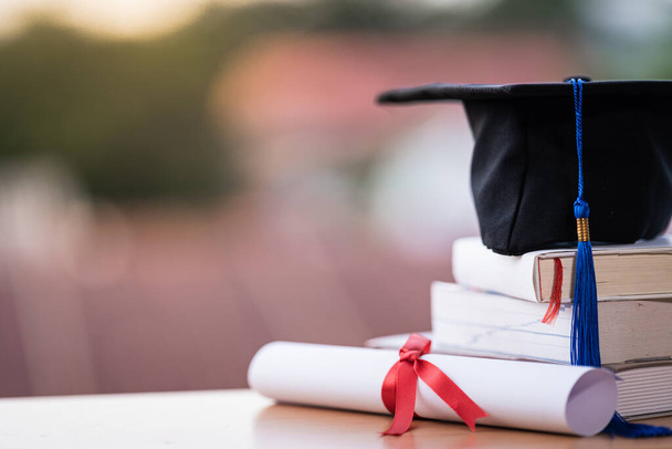Foto recortada de un sombrero de graduación universitaria mortero y diploma certificado de grado sobre la mesa - Foto, imagen