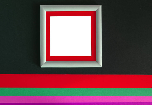 White wooden photo frame on a dark background and multi-colored sheets of paper. - Photo, Image