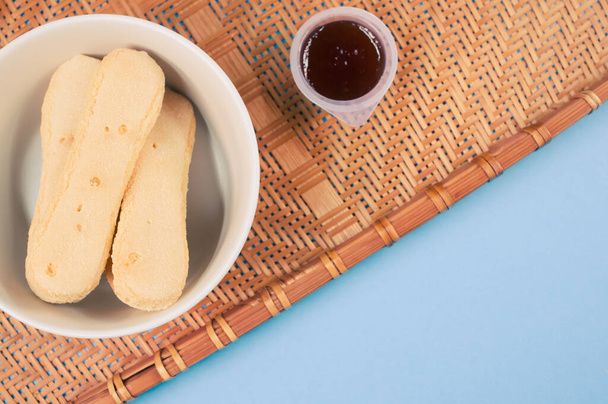 A top view of ladyfinger cookies with ketchup dip on a bamboo wicker tray isolated on blue background - Foto, immagini