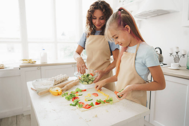 Close up of mother and daughter preparing vegan pizza in kitchen - Foto, Bild
