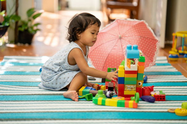 A closeup of a little girl playing with colorful construction toys on the floor. - Φωτογραφία, εικόνα