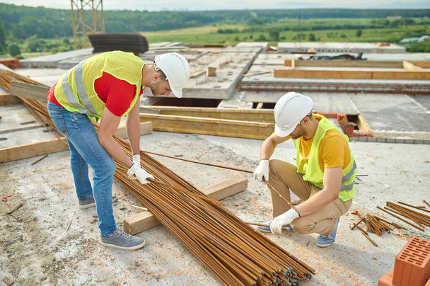 Experienced focused builders in cotton gloves selecting rebars - Fotografie, Obrázek