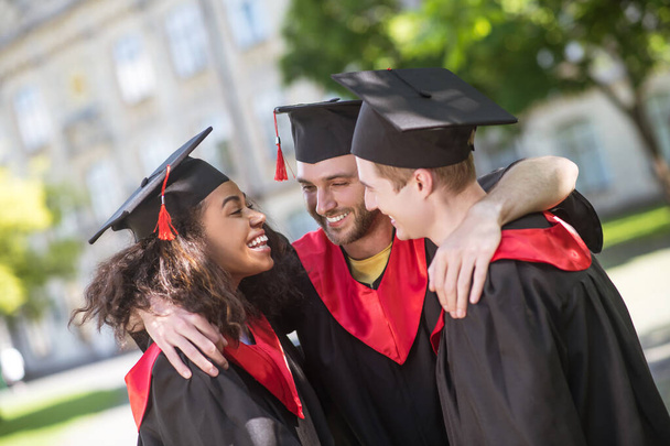 Three graduates hugging and discussing their graduation - Foto, Bild