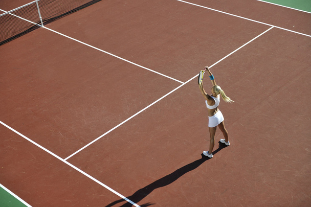 junge fitte Frau spielt Tennis im Freien auf orangefarbenem Tennisplatz am frühen Morgen - Foto, Bild