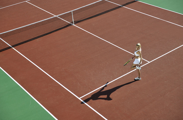 Young fit woman play tennis outdoor on orange tennis field at early morning - 写真・画像