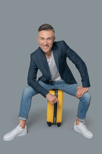 Smiling attractive man sitting on suitcase - Foto, imagen