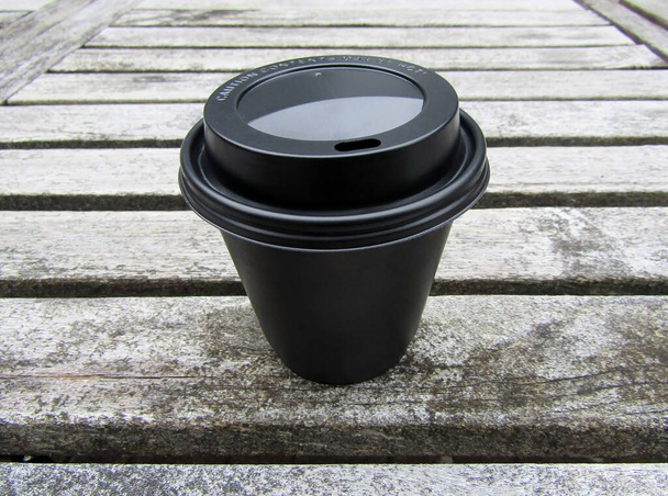 木製テーブルの上に黒のリサイクル可能な旅行蓋付きブラックペーパーコーヒーカップ - 写真・画像