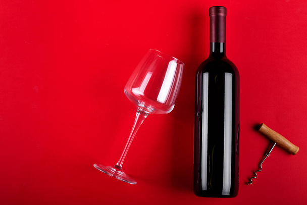 Bottle of red wine and an empty wine glass with a corkscrew next to it. Composition on a red background. Romantic mood. Space for text. Top view. - Foto, Bild