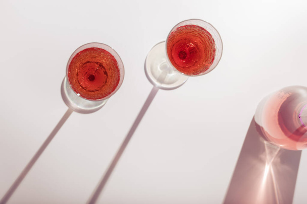 Рожеве вино в яскравих кришталевих окулярах, рожеве шампанське ігристе вино з денними світлими тінями. Літній алкогольний напій вид зверху, концепція виноробства
. - Фото, зображення