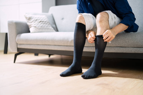Man Putting On Medical Compression Stockings On Legs - Foto, immagini