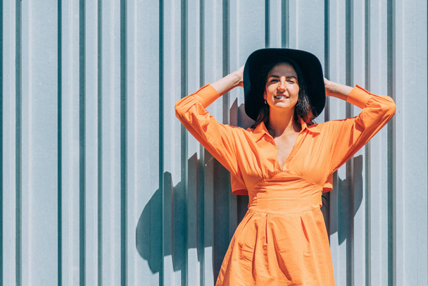 jeune fille à la mode en robe orange et chapeau sur fond de mur gris extérieur - Photo, image
