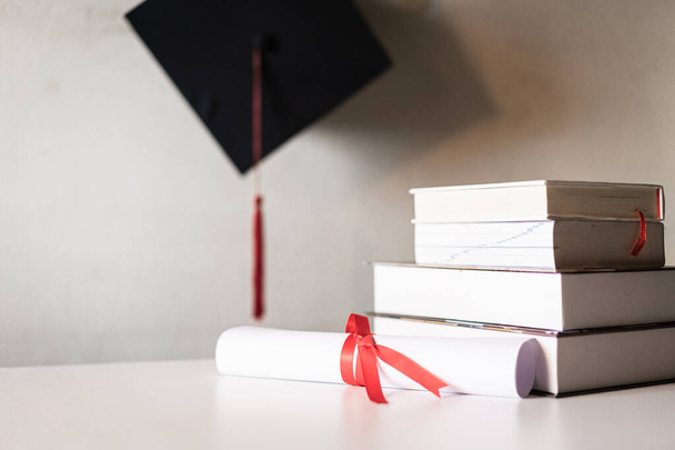 卒業用の帽子またはモルタルボードと卒業証書の証明書の紙は、空のスペースを持つ書籍の山の上に赤いリボンで結ばれ、ヴィンテージ効果のためにヴィネットでわずかに不飽和 - 写真・画像