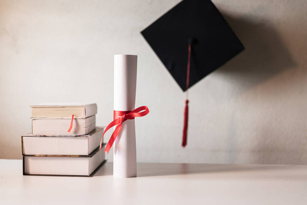 Un sombrero de graduación o un papel certificado de mortero y diploma atado con cinta roja en una pila de libros con espacio vacío ligeramente insaturado con viñeta para un efecto vintage. - Foto, imagen