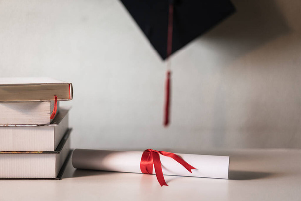 卒業用の帽子またはモルタルボードと卒業証書の証明書の紙は、空のスペースを持つ書籍の山の上に赤いリボンで結ばれ、ヴィンテージ効果のためにヴィネットでわずかに不飽和 - 写真・画像