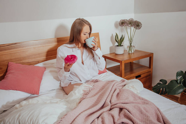Drinking coffee and eating doughnut for breakfast in bed - Фото, изображение