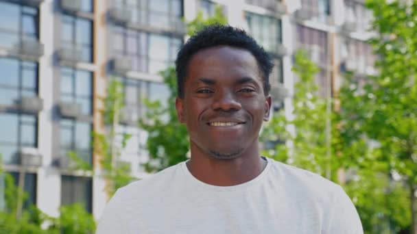 閉じる上の笑顔アフロアメリカ人男性見ますカメラオンバックグランド現代的な建物 - 映像、動画