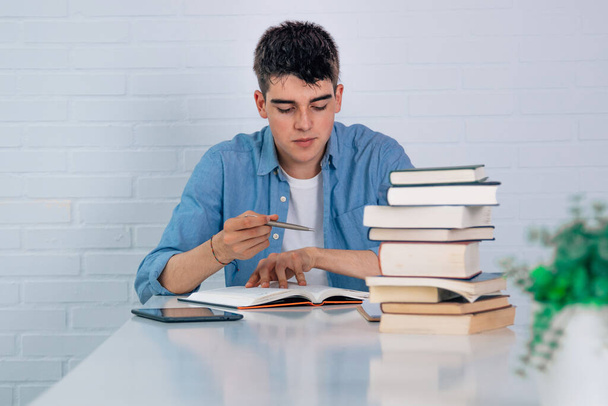 тинейджер за столом с книгами в стопке - Фото, изображение