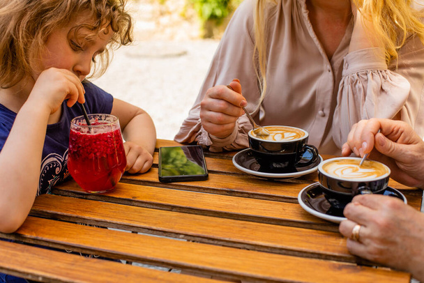 the little girl with mom and grandma drinks juice in a cafe - Фото, изображение