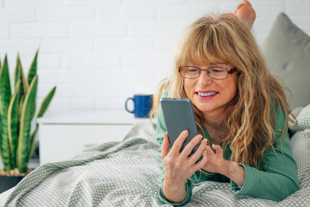 femme d'âge moyen avec téléphone portable au lit - Photo, image