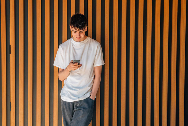 tiener jongen met mobiele telefoon op de straat muur - Foto, afbeelding
