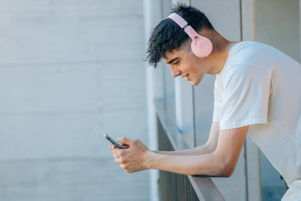dospívající chlapec s mobilním telefonem a sluchátky na balkóně - Fotografie, Obrázek