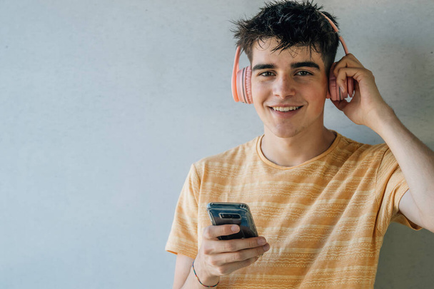 adolescent avec téléphone portable et écouteurs sur fond de mur gris - Photo, image