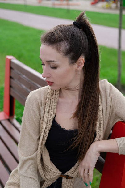 vonzó barna nő ül egy padon a parkban. divat ruhák, stílusos megjelenés. - Fotó, kép