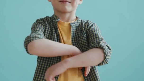 Slowmo kippen Porträt eines glücklichen 6-jährigen Jungen, der seine Arme verschränkt und vor blauem Hintergrund für die Kamera posiert - Filmmaterial, Video