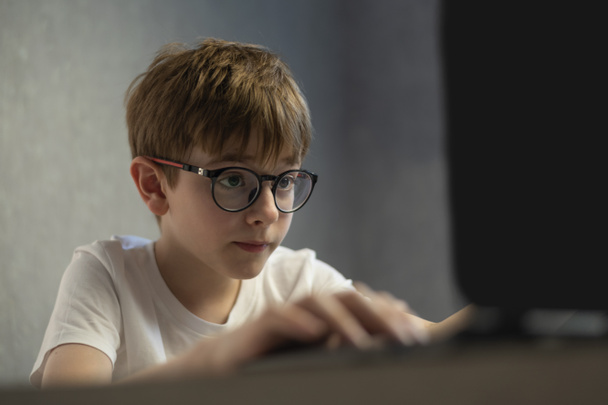 Boy in glasses joue avec enthousiasme à des jeux informatiques. Adolescent étudie en ligne. Préparation aux examens. - Photo, image