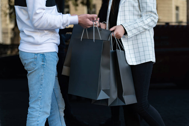 Mann und Frau halten schwarze Einkaufstüten in der Hand. Mädchen und Jungen treffen sich nach dem Einkaufen. Attrappe auf. Black-Friday-Konzept. - Foto, Bild