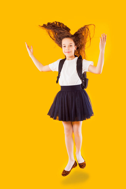 The happy little girl jumps on a yellow background - Фото, изображение