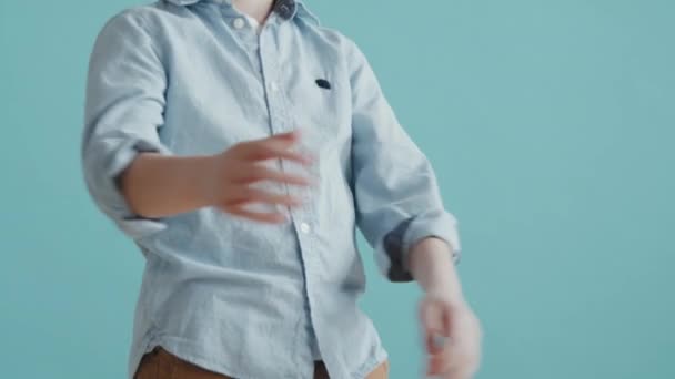 Obróć powoli ujęcie 6-letniego chłopca, który krzyżuje ramiona i odwraca wzrok od aparatu, pozując na niebieskim tle. - Materiał filmowy, wideo