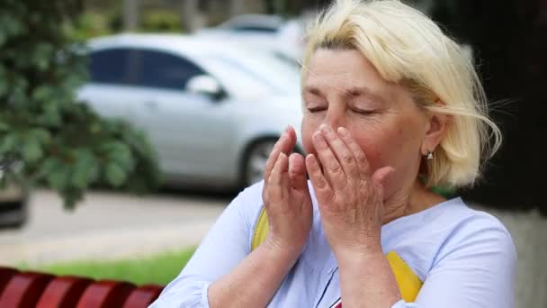 Allergie gegen Staub. Coronavirus Covid 19 Erwachsene blonde Frau niest, während sie draußen im Park sitzt. Allergie gegen Pflanzen und Blütenpollen. - Filmmaterial, Video