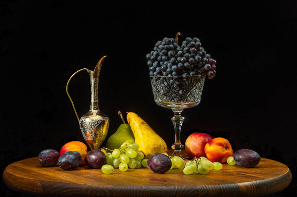 Bodegón con frutas sobre una mesa redonda de madera y fondo negro. - Foto, imagen