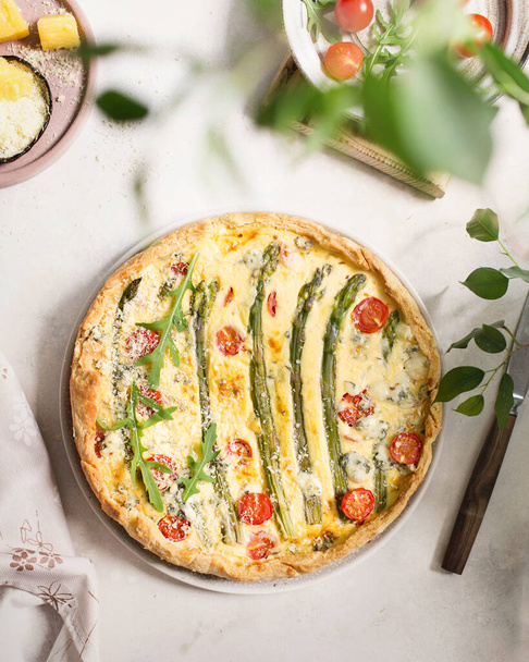 French cuisine. Quiche with asparagus, cherry tomatoes, and cheese. Summer food. Pie with cheese with blue mold and parmesan. Summer lunch on a light background. Pie made of fresh vegetables, arugula. - Photo, Image