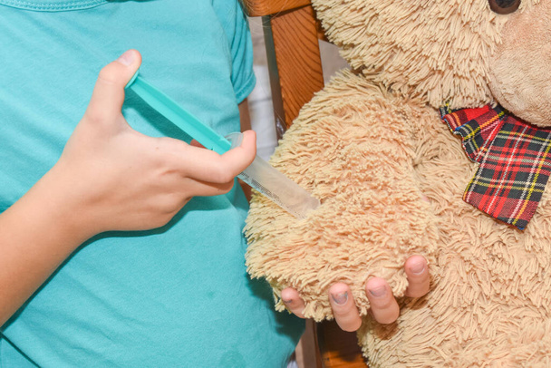 a child girl with a syringe makes an injection vaccination toy bear photo without processing - Zdjęcie, obraz