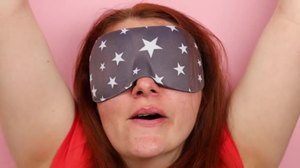 Portrét unavené dívky s maskou na spaní protáhnout po spánku v dopoledních hodinách izolované přes růžové pozadí. - Záběry, video