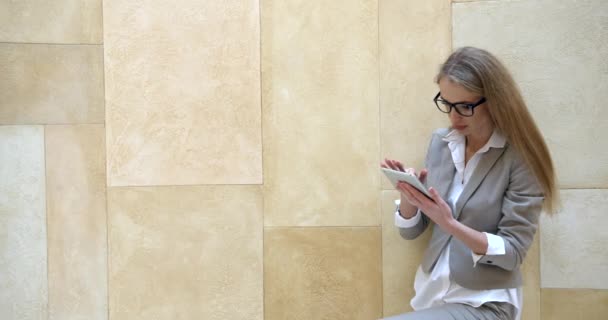 Portret van de jonge blonde zakenvrouw bedachtzaam en verrast tijdens het gebruik van de tablet aan de gele muur. - Video