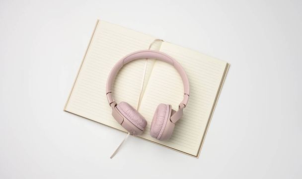 beige wireless headphones and a open notepad on a white background. Top view  - Photo, Image