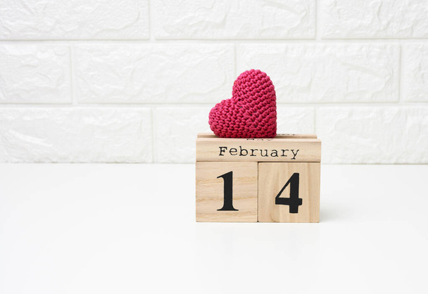 ξύλινο ημερολόγιο με ημερομηνία 14 Φεβρουαρίου και κόκκινη πλεκτή καρδιά, λευκό τραπέζι - Φωτογραφία, εικόνα