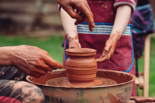 陶器の鍋を作る父と息子。家族は陶芸ホイールに取り組んでいます。ポッターと子供の手。外の陶芸工房。陶芸の車輪の上に作成するために子供を教えるマスター。職人の手と子 - 写真・画像