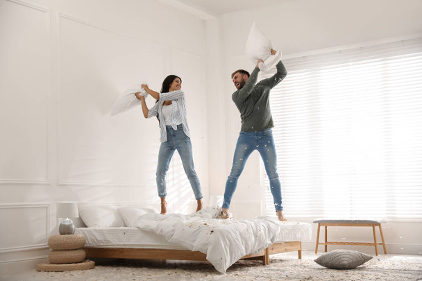 Happy young couple having fun pillow fight in bedroom - Zdjęcie, obraz