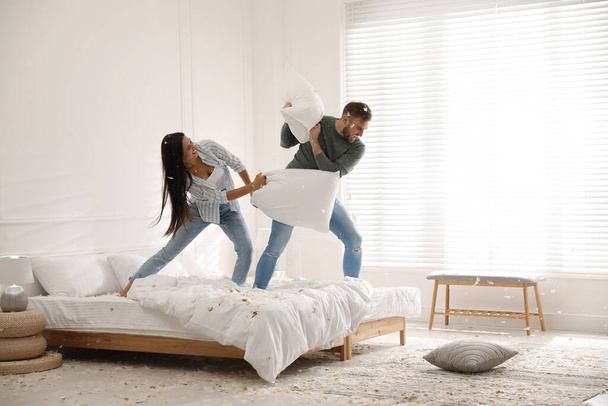Happy young couple having fun pillow fight in bedroom - Foto, imagen